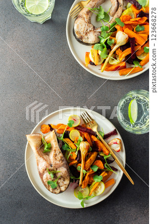 Baked silver carp with roasted carrots, zucchini, beets, and garlic , perfect for a healthy and delicious breakfast or lunch, plates with food on a dark background 123668278