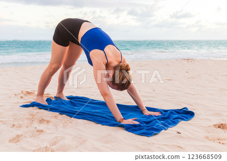 Young sporty blond girl does yoga on the beach, back stretching 123668509