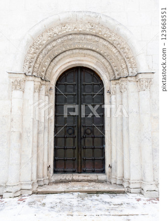 An old black metal door is in white wall of an ancient church, front view 123668551