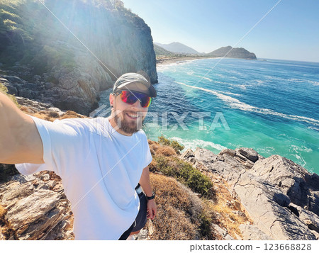 Man Taking Selfie on Rocky Cliff with Turquoise Sea View in Gazipasa Turkey on Sunny Day 123668828