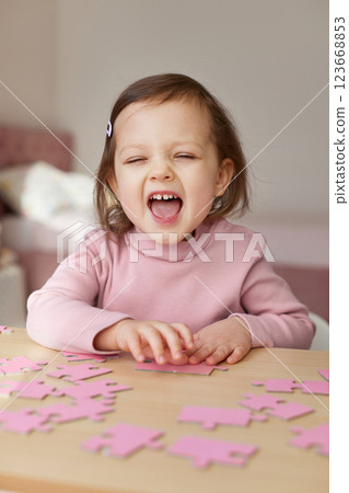 happy little child girl connecting puzzle pieces on wooden desk in room 123668853