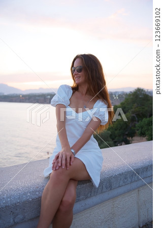 Relaxed woman in white dress sitting by the sea during sunset in Antalya 123669102