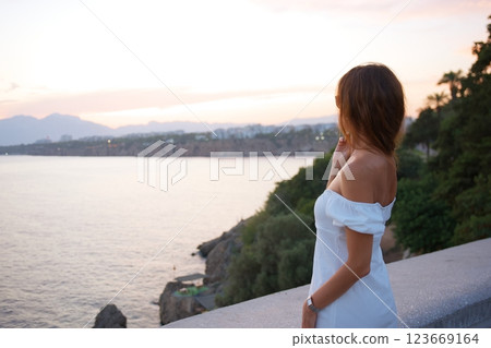 Woman in white dress enjoying sunset view over sea Woman in white dress enjoying sunset view over sea 123669164