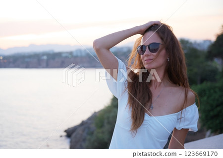 Confident woman in white dress posing by sea at sunset Confident woman in white dress posing by sea at sunset 123669170