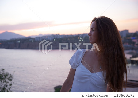 Elegant woman with long hair enjoying peaceful sunset view by the sea Elegant woman with long hair enjoying peaceful sunset view by the sea 123669172
