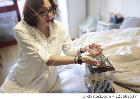 Woman holding her pet hamster in her hands over cage 123669537