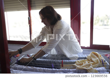 Woman hanging clothes on clothesline at home, managing household chores Woman hanging clothes on clothesline at home, managing household chores 123669556