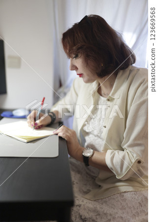 Businesswoman writing notes at home office desk 123669568