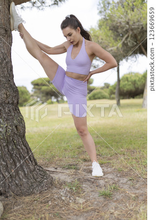 A Young Woman Gracefully Stretching and Enjoying the Sunny Day in the Park, Embracing the Warm Rays of the Sun 123669659