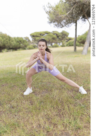 A Young Woman Gracefully Stretches Her Leg in a Scenic Park on a Beautiful, Sunny Day A Young Woman Gracefully Stretches Her Leg in a Scenic Park on a Beautiful, Sunny Day 123669764