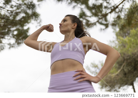 A Young Woman Showing off Her Strength by Flexing Her Biceps in a Beautiful Park on a Bright and Sunny Day 123669771