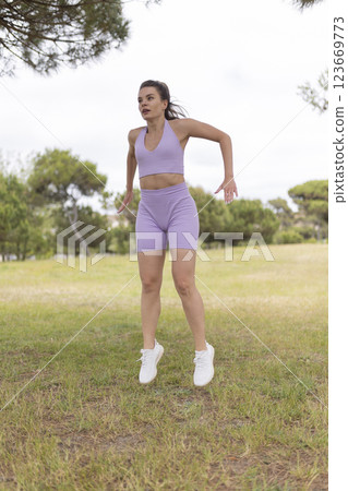 A Vibrant Young Woman Wearing Purple Sportswear Happily Jumping Around and Exercising in a Beautiful Park A Vibrant Young Woman Wearing Purple Sportswear Happily Jumping Around and Exercising in a Beautiful Park 123669773