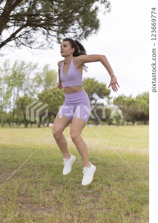 A Young Woman Energetically Jumping During Her Exercise Routine in a Beautiful Park on a Sunny Day A Young Woman Energetically Jumping During Her Exercise Routine in a Beautiful Park on a Sunny Day 123669774