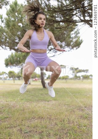 A Young Woman Joyfully Jumping in a Vibrant Park on a Sunny Day, Filled With Energy and Life 123669781