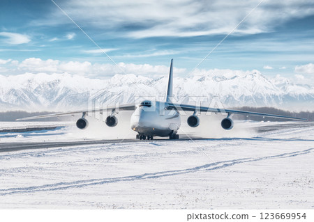 White big cargo airplane taxiing on the main taxiway at winter airport on the background of high snow capped mountains White big cargo airplane taxiing on the main taxiway at winter airport on the background of high snow capped mountains 123669954