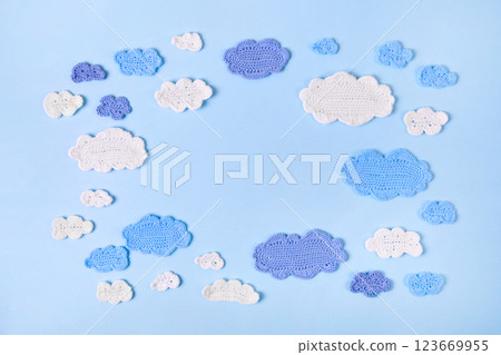 Knitted toys blue and white clouds on blue background. Baby stuff and accessories. Abstract knitted summer background. Top view, flat lay, copy space Knitted toys blue and white clouds on blue background. Baby stuff and accessories. Abstract knitted summer background. Top view, flat lay, copy space 123669955