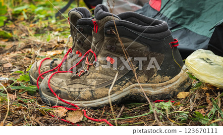 A pair of dirty hiking boots with red laces stands on a bed of fallen leaves and needles in the woods. Mountain hiking shoes. Close-up A pair of dirty hiking boots with red laces stands on a bed of fallen leaves and needles in the woods. Mountain hiking shoes. Close-up 123670111