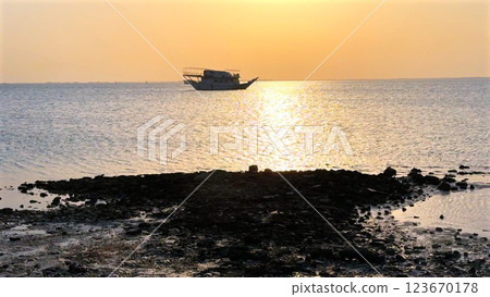 Traditional fishing boat floats gently beneath glowing horizon, golden light dances across gentle ripples, capturing peaceful essence of ocean at dusk with warm reflections. 123670178