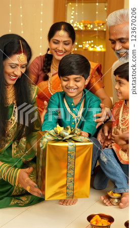 Indian family, dressed in traditional attire, gives wrapped presents to a delighted child during the diwali festival celebration in a decorated home setting 123670206