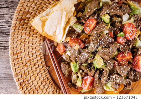 Tender beef stir fry with vegetables, sesame seeds arranged on woven platter with crispy tortillas nearby. Tender beef stir fry with vegetables, sesame seeds arranged on woven platter with crispy tortillas nearby. 123671045