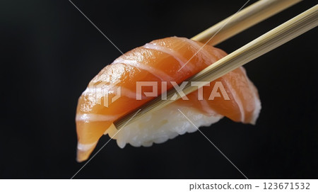 Sushi nigiri with fresh salmon held by chopsticks on black background, close up 123671532