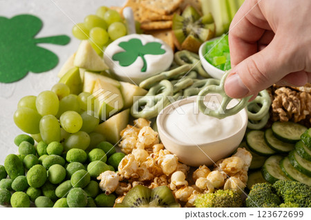 St Patricks day charcuterie board decorated shamrock and clover leaf. Festive holiday appetizer for celebration. Man hands dip cracker to sauce. Close up 123672699