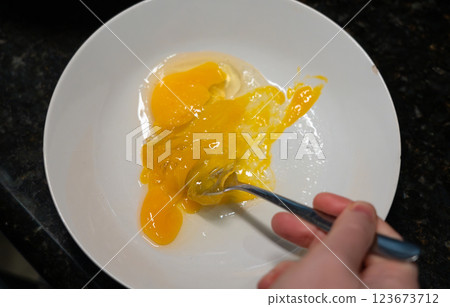Female hands beat eggs with fork in a bowl, homemade schnitzel cooking process closeup Female hands beat eggs with fork in a bowl, homemade schnitzel cooking process closeup 123673712