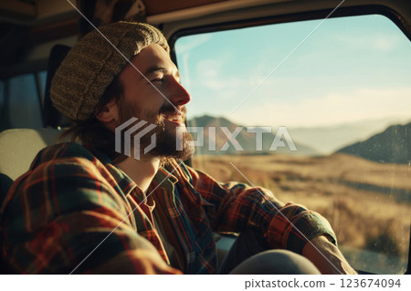 Content young man with a beanie hat smiles serenely while on a road trip, taking in the scenic desert landscape from his camper van Content young man with a beanie hat smiles serenely while on a road trip, taking in the scenic desert landscape from his camper van 123674094