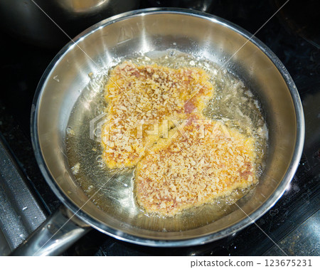 Frying schnitzel in hot oil in a steel pan, boiling oil with a piece of meat, cooking homemade schnitzel Frying schnitzel in hot oil in a steel pan, boiling oil with a piece of meat, cooking homemade schnitzel 123675231
