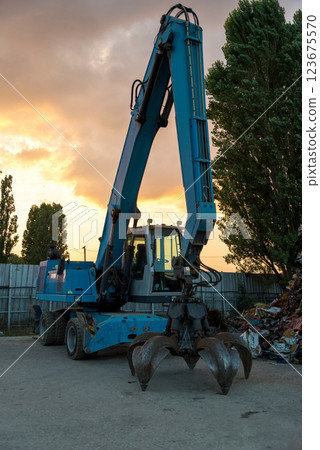A huge mechanical claw excavator used to load shredded metal at a scrapheap junkyard 123675570