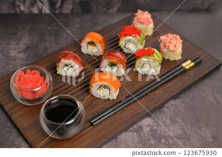 Set of sushi roll, ginger, soy sauce, chopsticks on serving board. Dark black texture background with copy space. Japan menu. Asian food Set of sushi roll, ginger, soy sauce, chopsticks on serving board. Dark black texture background with copy space. Japan menu. Asian food 123675930