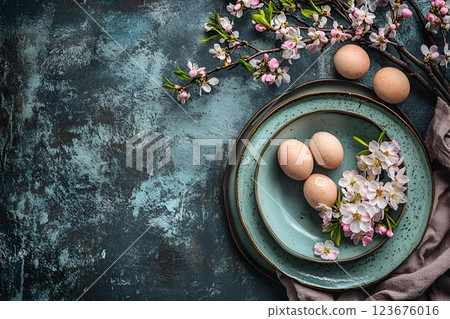 Rustic table setting with blue ceramic plates, quail eggs, and blossoming branches on a dark textured background Rustic table setting with blue ceramic plates, quail eggs, and blossoming branches on a dark textured background 123676016