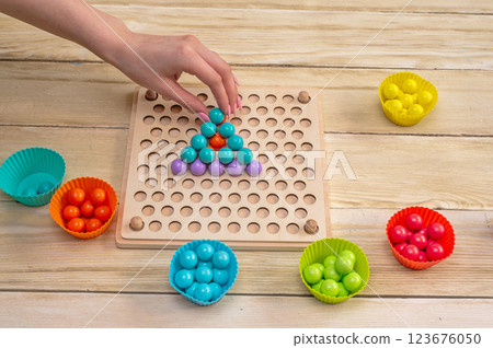 Educational game, wooden board for sorting according to the Montessori system. In her hands are wooden tweezers with a ball. Educational game, wooden board for sorting according to the Montessori system. In her hands are wooden tweezers with a ball. 123676050