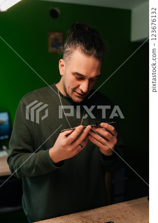Vertical portrait of professional computer master examining motherboard, troubleshooting issues in professional electronics repair workshop with green wall. Concept of computer hardware, repairing. 123676132