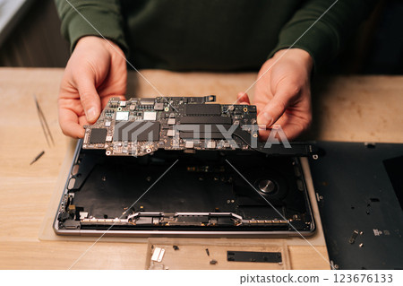 Closeup top view of electronic technician inspecting delicate laptop motherboard component, diagnostic process underway in specialized repair workshop. Concept of process electronic device repair. 123676133