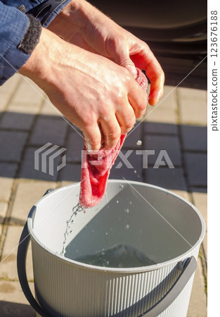 Man Squeeze Water from hands and washing wipe into Bucket Outdoors on Sunny Day. High quality photo 123676188