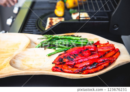 Delicious grilled vegetables asparagus, paprika on barbecue grill with smoke and flame. Asparagus and red paprika on the wooden plate. 123676231