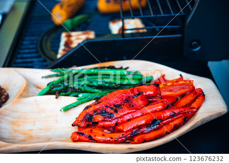 Delicious grilled vegetables asparagus, paprika on barbecue grill with smoke and flame. Asparagus and red paprika on the wooden plate. Delicious grilled vegetables asparagus, paprika on barbecue grill with smoke and flame. Asparagus and red paprika on the wooden plate. 123676232