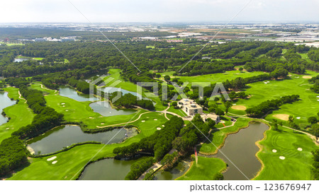 Panoramic aerial view of a golf course with lakes, sand bunkers, and a clubhouse surrounded by greenery Panoramic aerial view of a golf course with lakes, sand bunkers, and a clubhouse surrounded by greenery 123676947