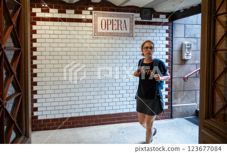 Budapest, Hungary, August 30, 2022. Old Opera metro station. Detail of the sign with the name of the station on the wall covered with tiles in excellent condition. A middle-aged woman is entering. Budapest, Hungary, August 30, 2022. Old Opera metro station. Detail of the sign with the name of the station on the wall covered with tiles in excellent condition. A middle-aged woman is entering. 123677084