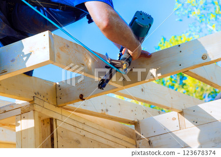 Carpenter works diligently, using air pneumatic nail gun to secure wooden beams during construction under construction 123678374