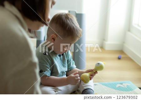 The child is sitting calmly playing with a toy, next to his mother 123679302