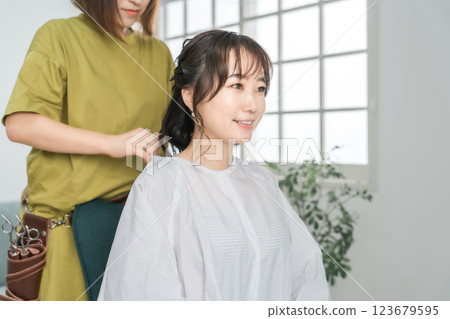 Hairdresser / barber Asian woman wearing a cross cape to a customer who came to a beauty salon / hair salon Hairdresser / barber Asian woman wearing a cross cape to a customer who came to a beauty salon / hair salon 123679595