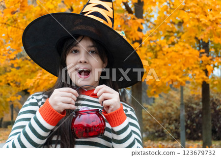 Excited child in witch hat holding candy pail amidst vibrant autumn leaves 123679732