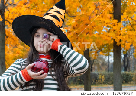 Young witch holding candy eye in autumn park during halloween 123679737