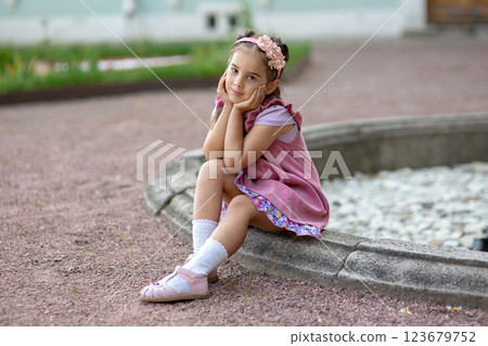 Young caucasian girl in pink dress sitting by fountain in garden Young caucasian girl in pink dress sitting by fountain in garden 123679752