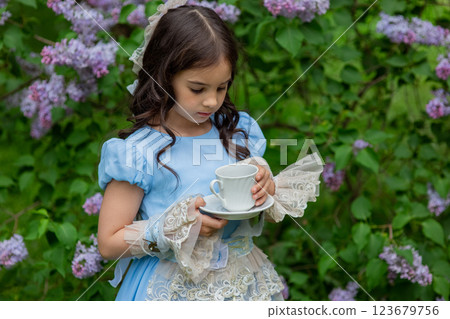 Caucasian child in blue dress enjoying tea in garden with lilac flowers Caucasian child in blue dress enjoying tea in garden with lilac flowers 123679756