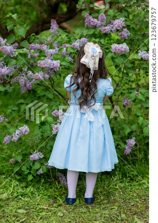 Young caucasian girl in blue dress among lilac flowers in garden Young caucasian girl in blue dress among lilac flowers in garden 123679757