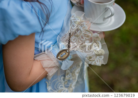 Young girl in blue victorian dress holding teacup in garden setting Young girl in blue victorian dress holding teacup in garden setting 123679819
