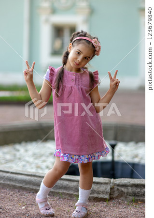 Young caucasian girl posing with peace signs in pink dress outdoors 123679840